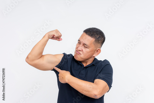 A cocky and self-assured middle-aged man showcases his strength by flexing and pointing at his biceps, against a white backdrop.