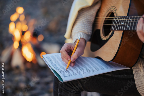 Girl composer playing the guitar composing new song outdoors near bonfire. Playing the guitar in autumn park in the evening, making new composition photo