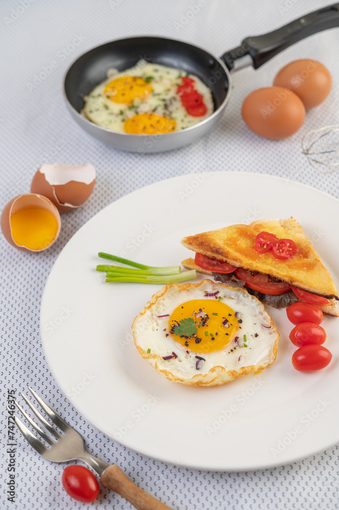 Fried egg on a white plate with toast, sliced ​​Spring onion and sliced ​​tomatoes