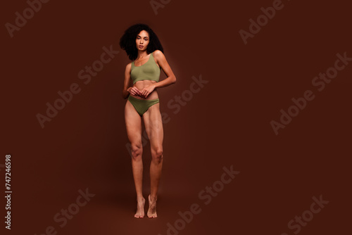 No filter photo of charming girl flawless athletic body thin waist standing barefoot empty space isolated on brown color background