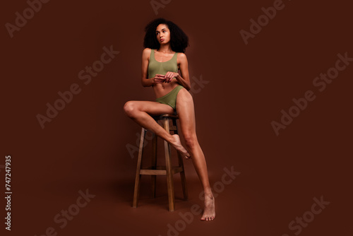 No filter photo of gorgeous woman wearing comfort activewear sitting stool posing empty space isolated on brown color background