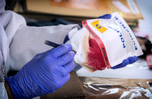 Forensic investigator removes from evidence bag some gauze impregnated with blood of murder victim at crime lab, conceptual image