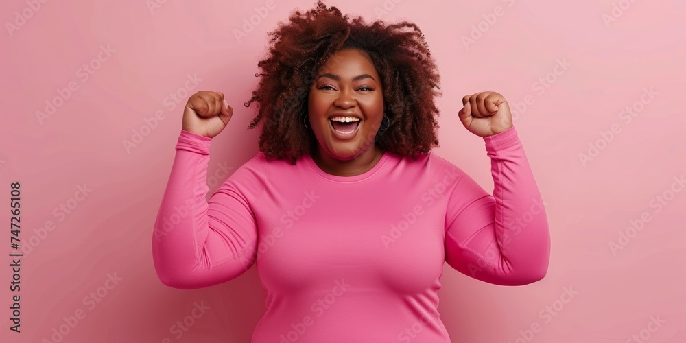 A joyful and attractive black woman celebrates success with a winning gesture and a cheerful smile. - obrazy, fototapety, plakaty 