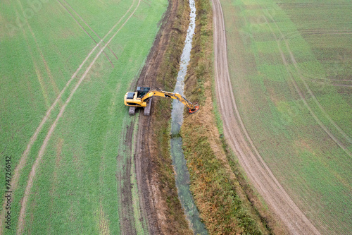 Drone photography of excavator cleaning drainage ditch in an agriculture field during autumn morning