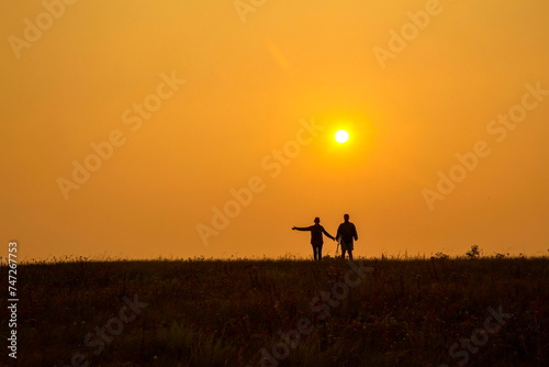 two silhouettes of two tourists in love against the background of an evening sunset in the mountains