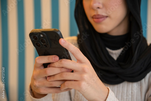 Young woman in hijab using phone in cafe