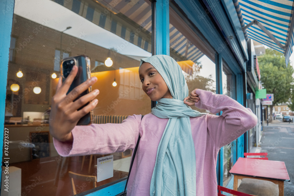 Young woman in hijab taking selfie in front of cafe