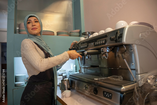 Young woman in hijab making coffee in cafe