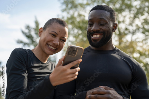 Smiling athletic man and woman looking at smart phone in park