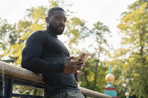 Athletic man with smart phone on footbridge in park