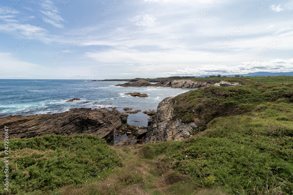 rocky cove surrounded by green field on the coast of asturias in summer