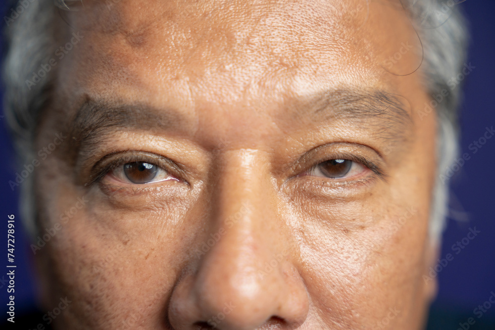 Close-up of senior man looking at camera against purple background Close-up of senior man looking at camera against purple background