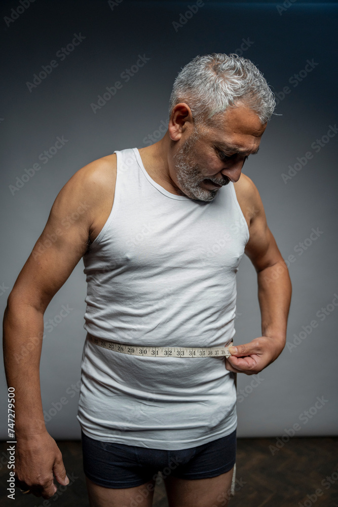 Portrait of man measuring waist against gray background Portrait of man measuring waist against gray background