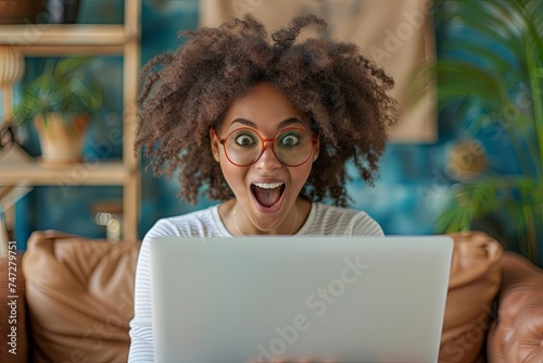 A joyful young woman in a business suit expresses excitement while holding her laptop.