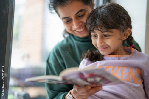 Canvas Print Mother and daughter reading book near window