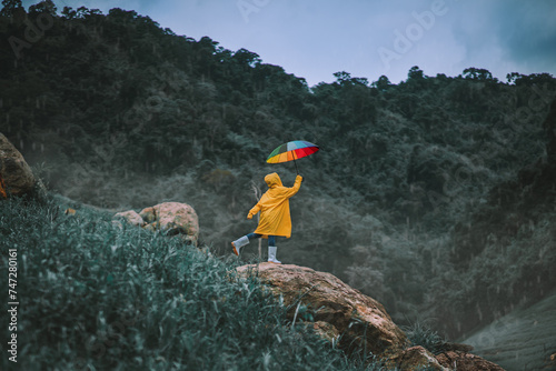 Woman in raincoat holding rainbow umbrella in green forest