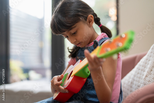 Little girl playing on ukulele in living room