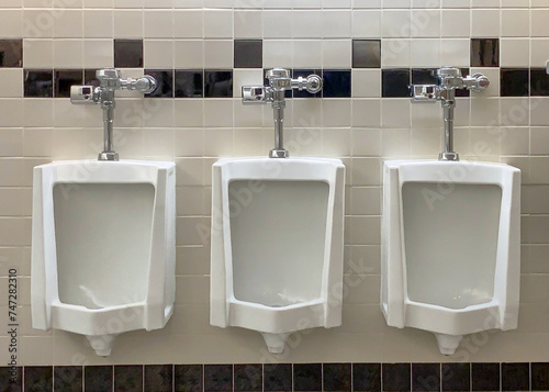 Three urinals in a row on a while with checkered wall tile photo