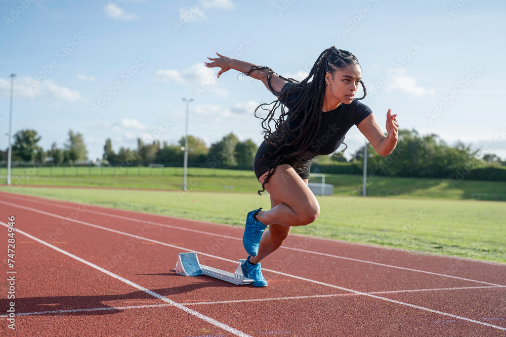 Obraz premium Female athlete sprinting off starting line at stadium