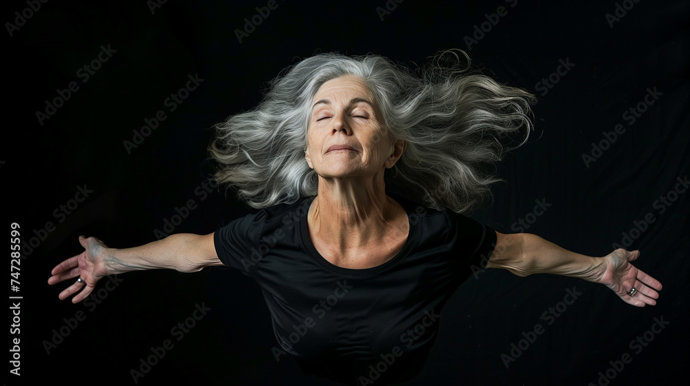 Mature woman with arms outstretched, silver hair flowing, eyes closed. Surrendering