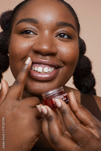 Studio shot of smiling young woman applying lip moisturizer