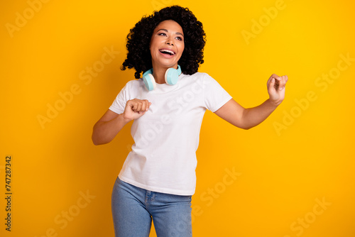 Photo of excited positive lady dressed white t-shirt enjoying music headphones dancing looking empty space isolated yellow color background