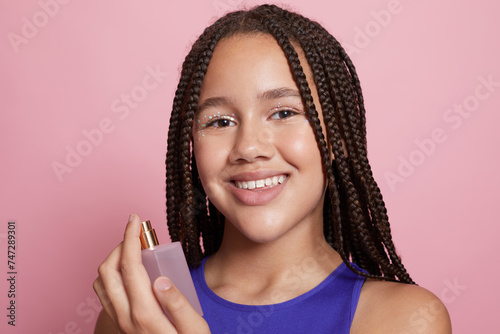Studio portrait of smiling girl spraying perfumes on neck