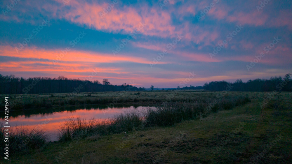 Sunset above the forest. Reflections of red clouds in the water of the lake. Bright colors at the end of the day during fall season Sunset above the forest. Reflections of red clouds in the water of the lake. Bright colors at the end of the day during fall season