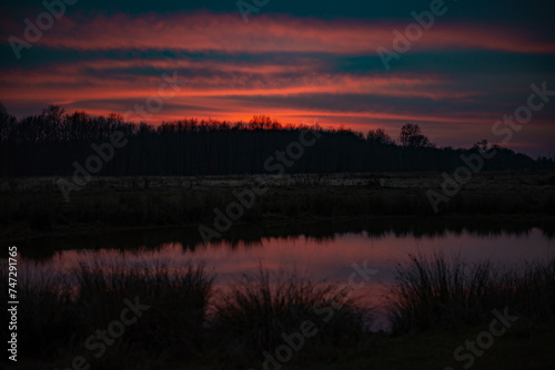 Sunset above the forest. Reflections of red clouds in the water of the lake. Bright colors at the end of the day during fall season