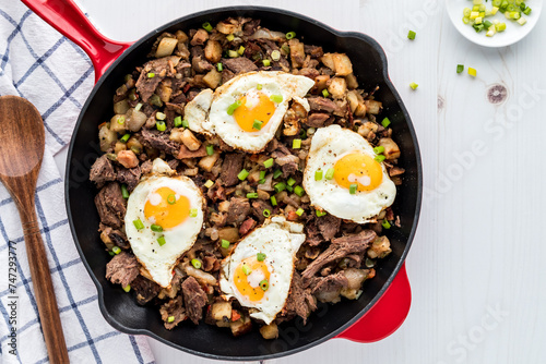 A frying pan of roast beef hash topped with fried eggs, ready for serving.
