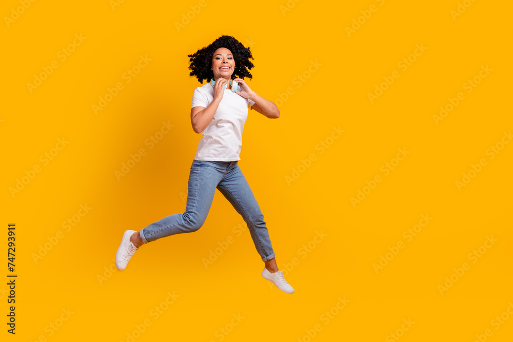 Full length photo of funky pretty lady dressed white t-shirt jumping enjoying music headphones empty space isolated yellow color background Full length photo of funky pretty lady dressed white t-shirt jumping enjoying music headphones empty space isolated yellow color background