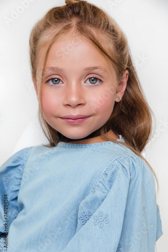 Portrait of cute blonde kid girl in blue dress on white studio background. Soft focus
