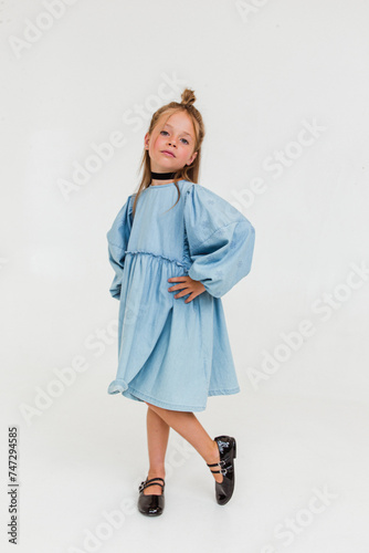 Happy cute little girl in blue dress smiling and posing on white background. Soft focus