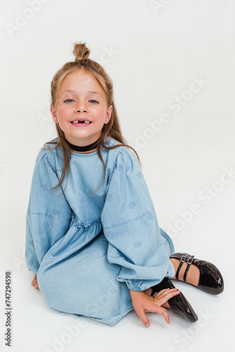 Little cute girl model in beautiful blue dress is sitting on white background. Soft focus