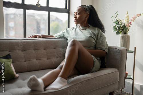 Free Download Portrait of young woman looking through window while resting on sofa at home - GFXLoad