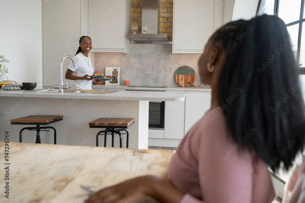 Smiling woman serving dinner for girlfriend at home