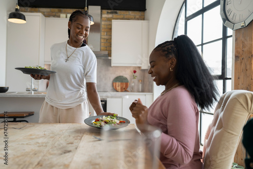 Smiling woman serving dinner for girlfriend at home