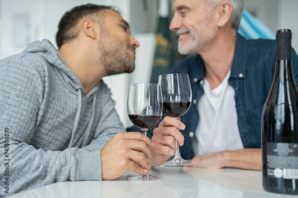 Male couple drinking red wine and kissing at home Male couple drinking red wine and kissing at home