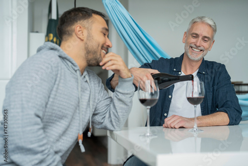Male couple pouring red wine at home
