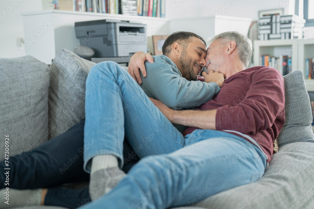 Smiling male couple cuddling on sofa at home Smiling male couple cuddling on sofa at home