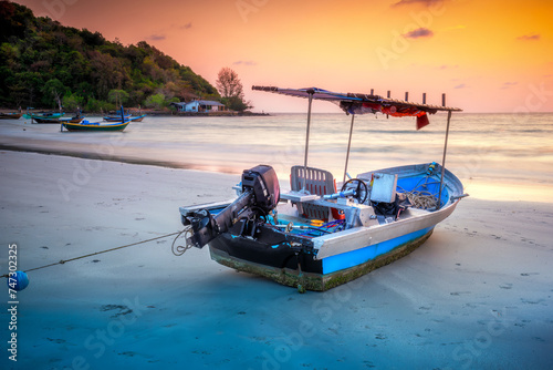 Thai fishing boat at sunset and low tide, Mae Ramphueng Beach, Rayong Province, Thailand.