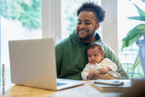 Father holding baby daughter and using laptop at home