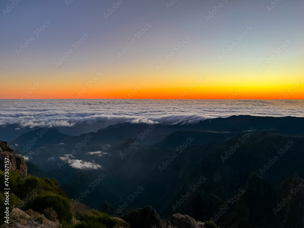 Panoramic view of sunrise seen from top Pico do Areeiro, Madeira island, Portugal, Europe. First sunlight touching surface of illuminated clouds covering the Atlantic Ocean. Dramatic red orange sky