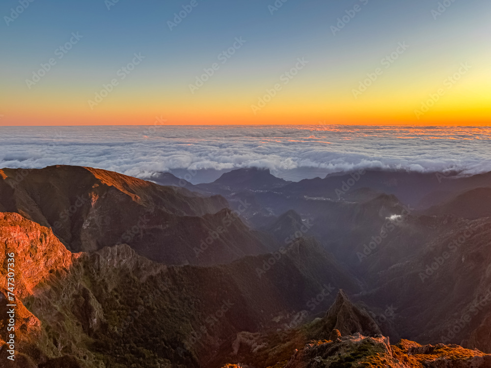Panoramic view of scenic valley and hills at sunrise seen from top Pico do Areeiro, Madeira island, Portugal, Europe. First sunlight touching unique misty landscape. Atlantic Ocean covered by clouds