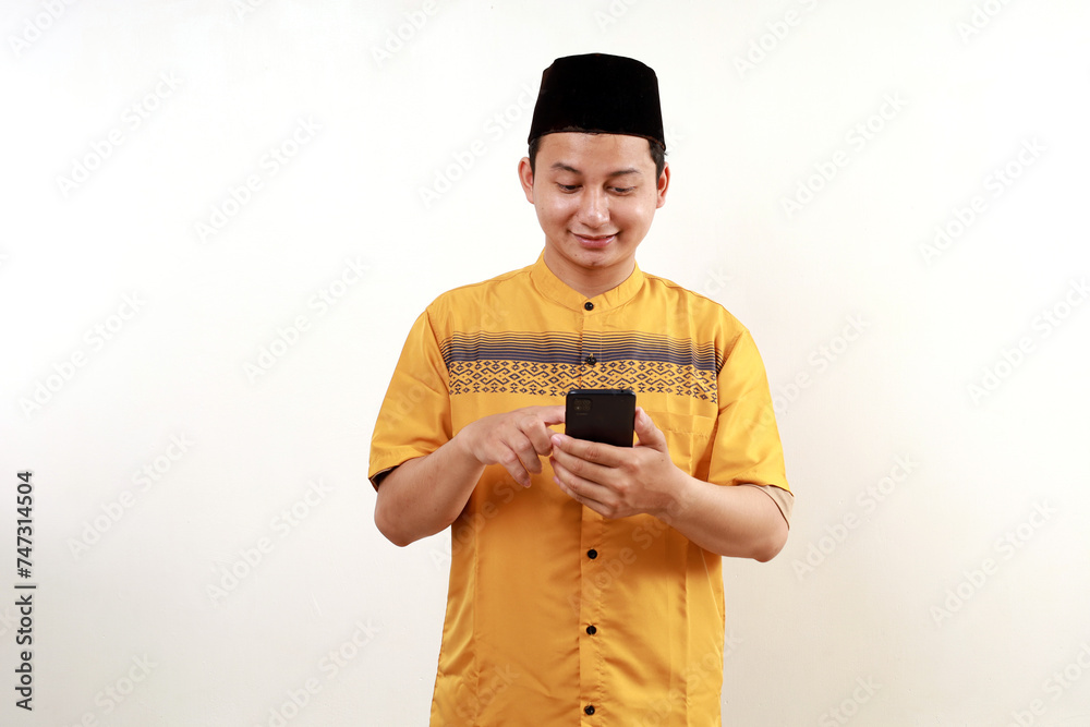 Portrait of young asian muslim man standing while using cell phone. Isolated on white Portrait of young asian muslim man standing while using cell phone. Isolated on white