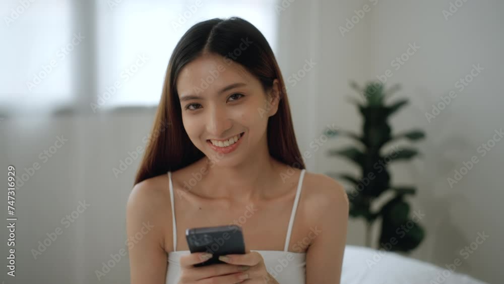 Beautiful woman using smartphone for checking notification social application on the bed in the morning. Happy asian female checking work schedule on apps smartphone and ready to start new day. Beautiful woman using smartphone for checking notification social application on the bed in the morning. Happy asian female checking work schedule on apps smartphone and ready to start new day.