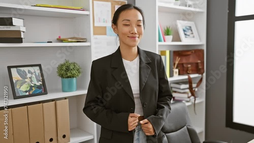 A professional asian woman in a blazer stands confidently in an office, personifying career-focused elegance. photo