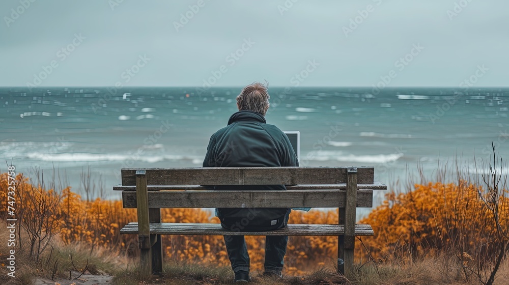Solo Man traveler gazes at ocean, sitting at wooden table with laptop, working remotely, a beautiful North landscape on the background Solo Man traveler gazes at ocean, sitting at wooden table with laptop, working remotely, a beautiful North landscape on the background