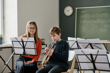 Young Caucasian female music teacher listening to middle school student playing trumpet during class