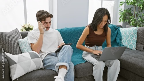 A man and woman, evidently a couple, are busy with technology in a cozy, modern living room setting. photo